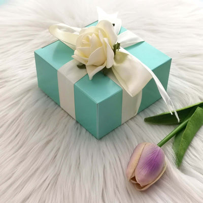 Turquoise gift box with white ribbon and rose, accompanied by a tulip.
