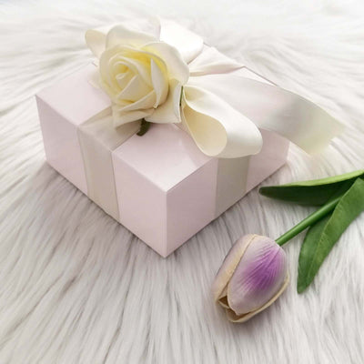 Pink gift box with white ribbon and rose, accompanied by a purple tulip.