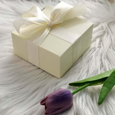 Elegant cream gift box with ribbon and a purple tulip on soft white fur.