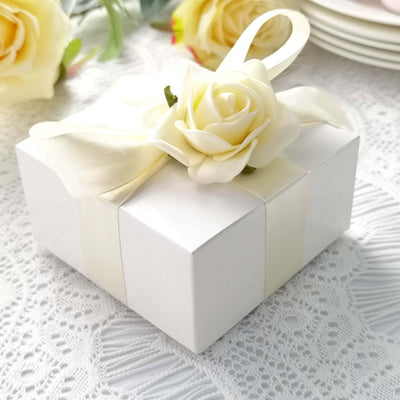 White gift box with a cream ribbon and rose decoration on a lace tablecloth.