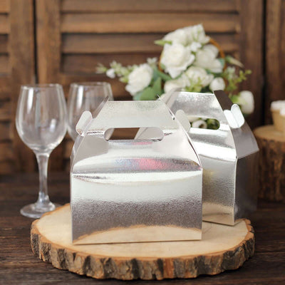 Silver gift boxes on a wooden slice with wine glasses and flowers in the background.