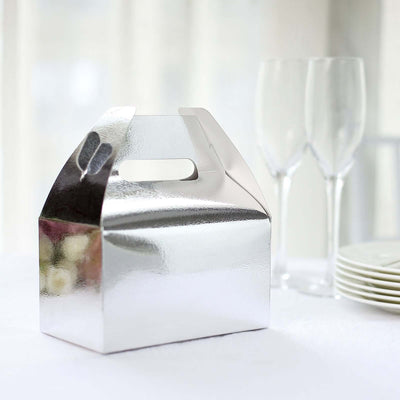 Silver gift box with handle on a table next to glasses and plates.