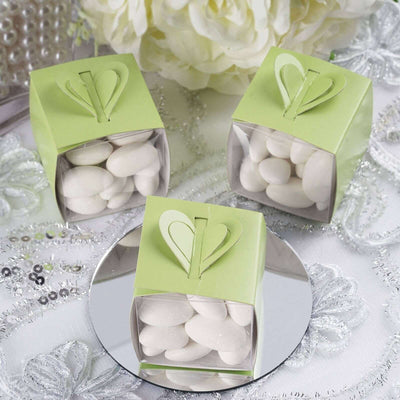 Green favor boxes filled with white candies, styled elegantly on a mirrored surface.
