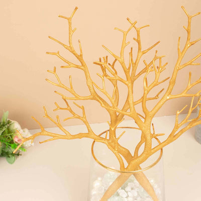 Gold decorative tree branches in a clear vase with white pebbles.