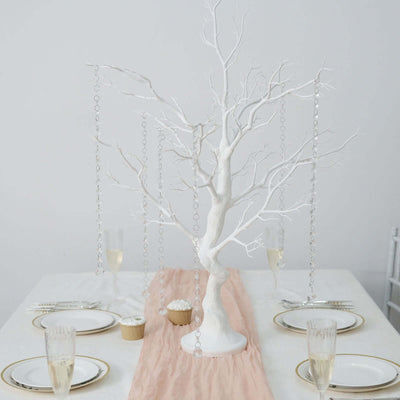 White decorative tree centerpiece with hanging crystals on a dining table.