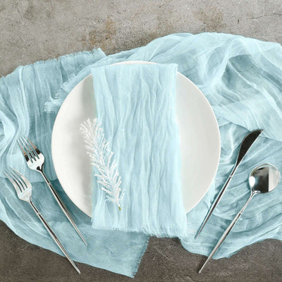 Elegant blue linen napkin on a white plate with silver utensils on a textured surface.