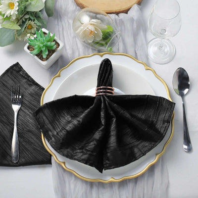 Elegant black napkin folded with a ring on a decorative plate, set for dining.