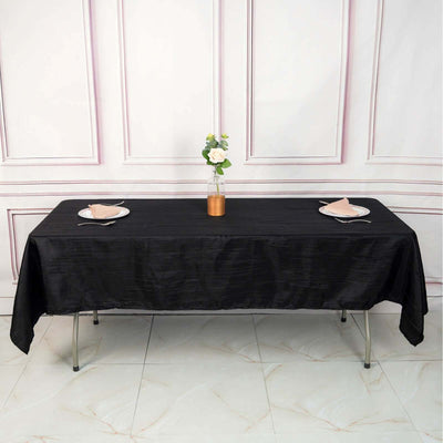 Black tablecloth set with plates and a vase on a styled table.
