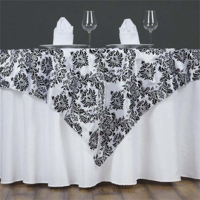 Black and white floral tablecloth draped over a round table with dinnerware.