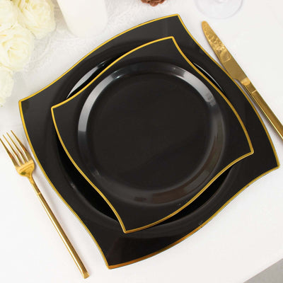 Black dinner plates with gold trim stacked on a white table setting.