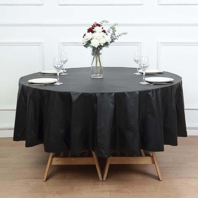 Black round tablecloth draped over a table set with plates and glasses.