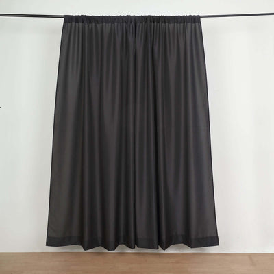 Sheer black curtain hanging on a rod against a plain backdrop