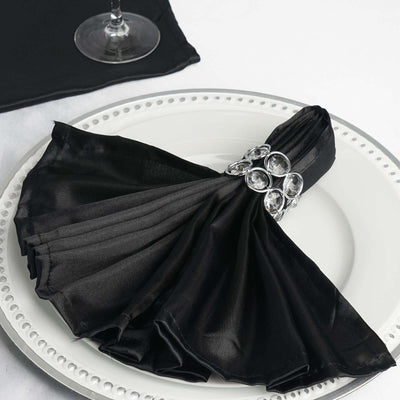 Black satin napkin elegantly folded with a crystal napkin ring on a white plate.
