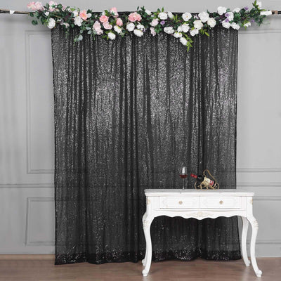Black sequin curtain with floral garland above a white table.