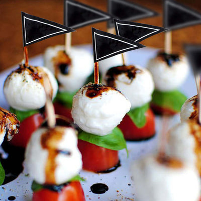 Caprese skewers with mozzarella, basil, and tomatoes topped with black flag markers.