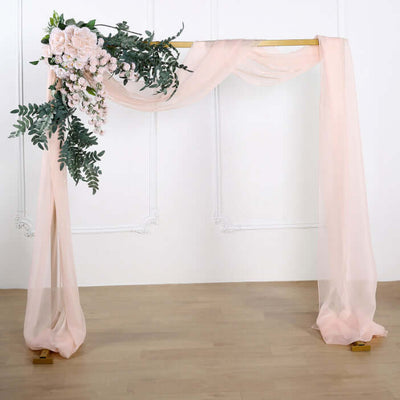 Floral draped wedding arch with soft pink fabric and greenery accents.