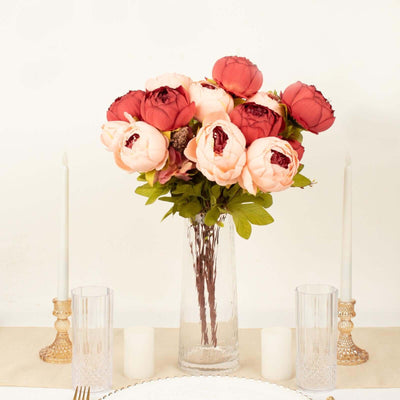 Bouquet of pink and red peonies in a clear glass vase on a table.