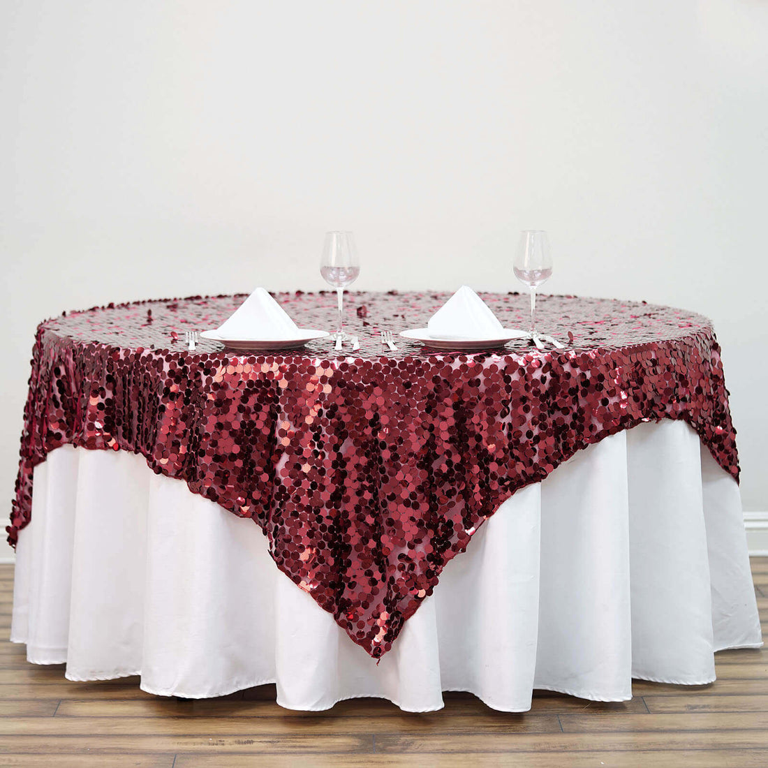 Round table with burgundy sequin tablecloth and wine glasses.