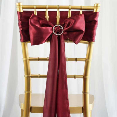 Burgundy satin chair sash with a bow and ring detail on a gold chiavari chair