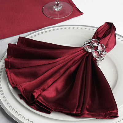 Burgundy satin napkin elegantly styled with a jeweled napkin ring on a plate.