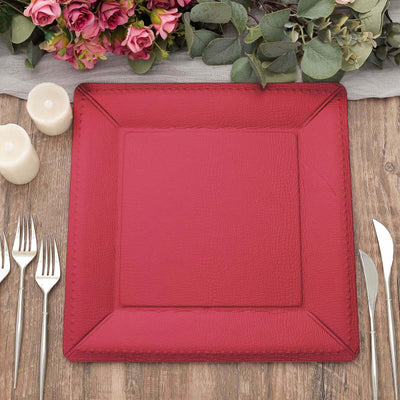 Red square leather placemat on a wooden table with cutlery and candles.