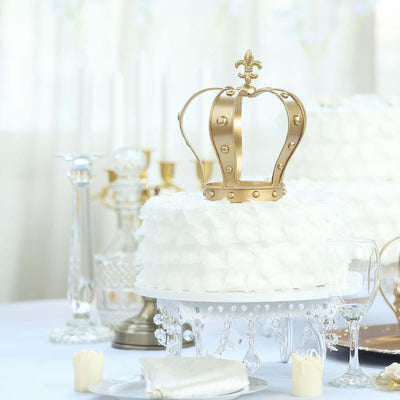 Elegant white cake with a gold crown topper on a decorated table.