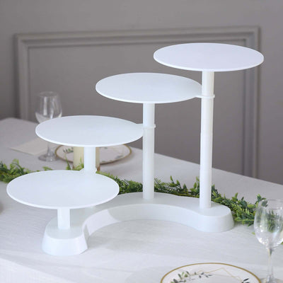White multi-tier cake stand on a table with greenery and plates