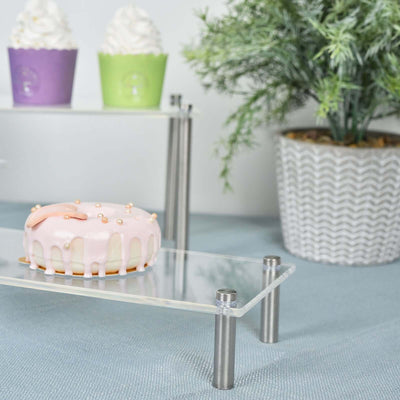 Pink frosted donut on a clear acrylic display stand with cupcakes in the background.