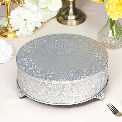 Silver cake stand with intricate floral design on a neutral tablecloth.