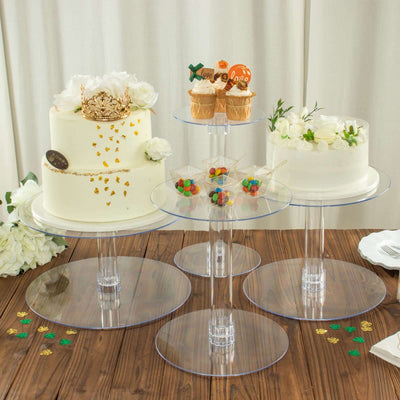 Three clear acrylic cake stands displaying decorated cakes and cupcakes on a wooden table.