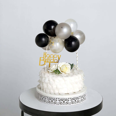 Birthday cake with black, white, and silver balloons on a table.