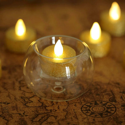 Gold glitter LED candle in a glass holder on a decorative surface.