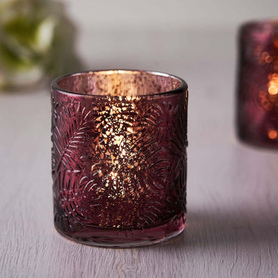 Purple etched glass candle holder with warm, flickering light.