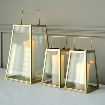 Set of three elegant glass lanterns with gold frames and candles inside.