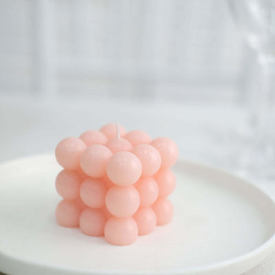 Pink bubble candle on a white plate against a light backdrop