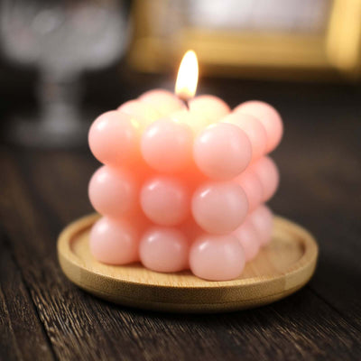 Pink bubble candle on a wooden plate with a soft glow.