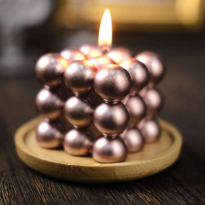 Rose gold decorative candle in a wooden dish with a flame.