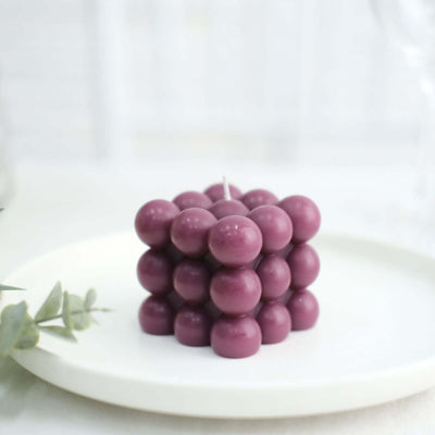 Purple bubble candle on a white plate with greenery in the background.