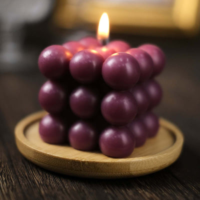 Purple bubble candle on a wooden tray, softly glowing with a warm flame.