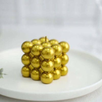 Gold spherical candle arranged in a cube shape on a white plate.