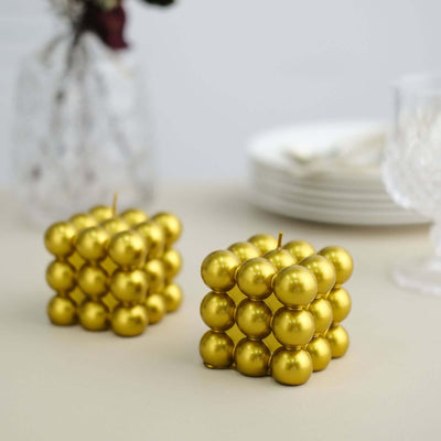 Gold geometric candle holders in cube shapes on a neutral surface.