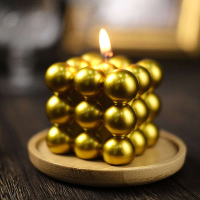 Gold sphere candle on a wooden plate, glowing warmly.
