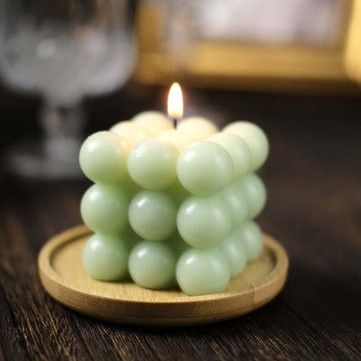 Green bubble candle on a wooden tray with a lit flame.