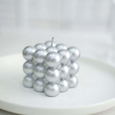 Silver spherical candle arranged in a cube shape on a plain white plate.
