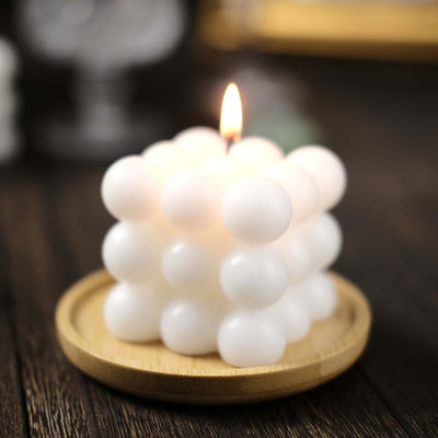 White bubble candle on a wooden plate with a lit wick.