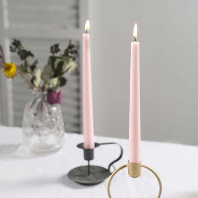 Pink taper candles in stylish holders on a table with a vase of dried flowers.