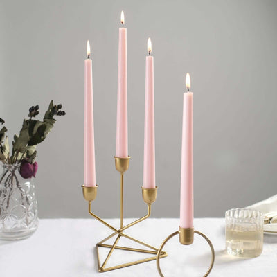 Pink taper candles in a gold holder with lit flames. Elegant home decor piece.