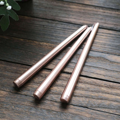 Set of three rose gold metallic pens on a wooden surface.