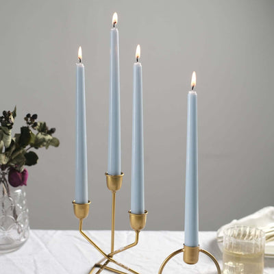 Blue taper candles in a gold holder with flames, set on a table.