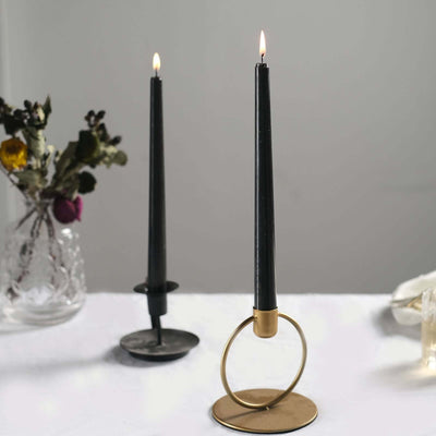 Black candlesticks in modern holders with lit candles on a table.